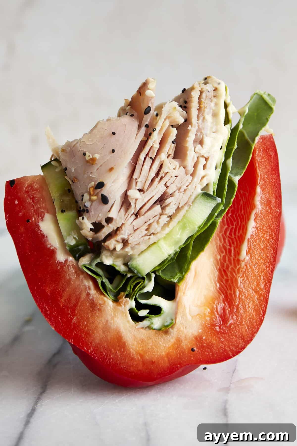 Side view of a perfectly halved low-carb turkey bell pepper sandwich, showcasing layers of turkey, cucumber, lettuce, and hummus, ready to eat.