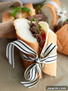 A delicious beef po'boy sandwich, wrapped elegantly in a black and white striped ribbon, showcasing the tender beef filling and fresh toppings.