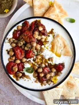 A creamy whipped feta dip topped with roasted cherry tomatoes and crispy chickpeas, garnished with fresh herbs, ideal for dipping.