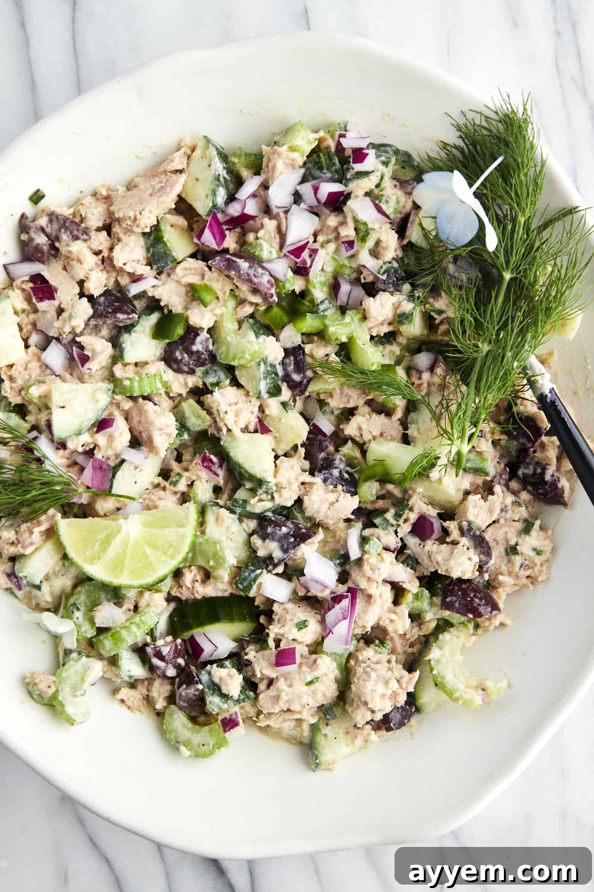 A bowl of Mediterranean tuna salad topped with fresh dill and lime wedges, ready to serve.
