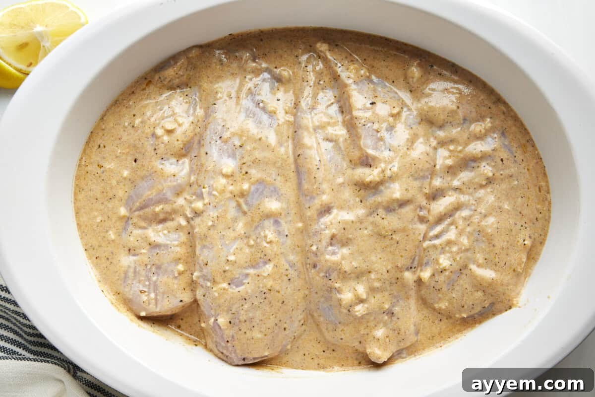 Classic Greek Lemon Chicken 3 Chicken breasts being marinated in a creamy Greek yogurt sauce, absorbing rich flavors.