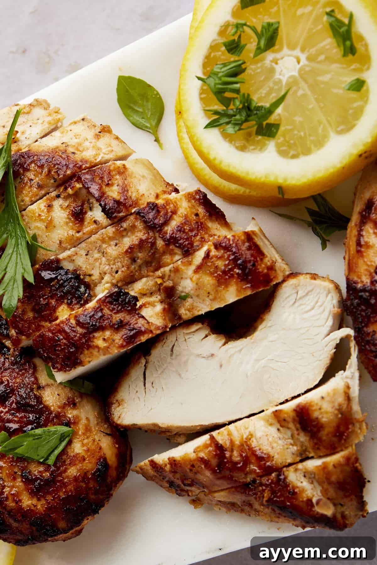 Classic Greek Lemon Chicken 5 Perfectly sliced Greek lemon chicken on a wooden cutting board, garnished with fresh herbs, ready to be served.