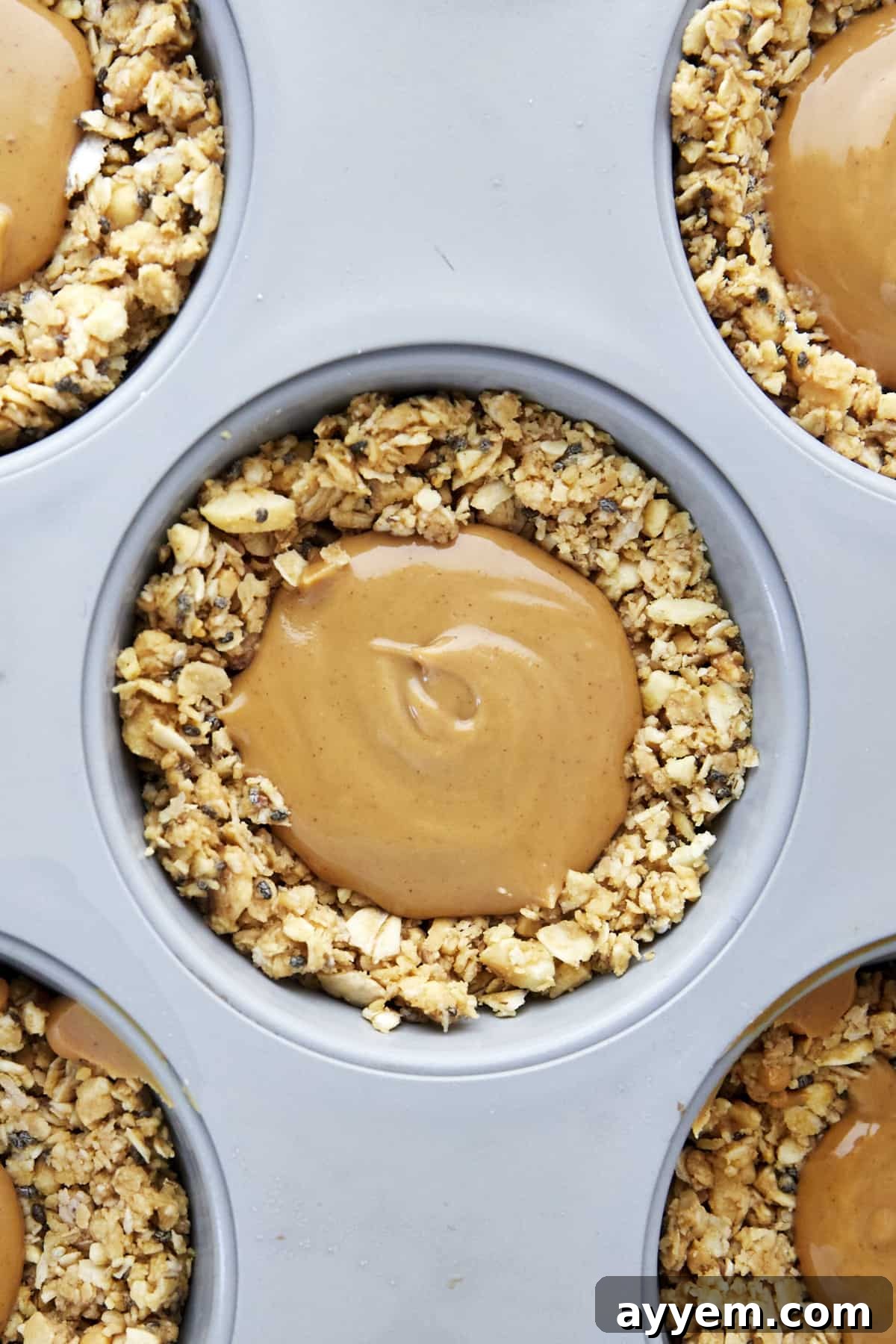 An individual oat cup base in a muffin tin with a dollop of creamy peanut butter filling in the center.
