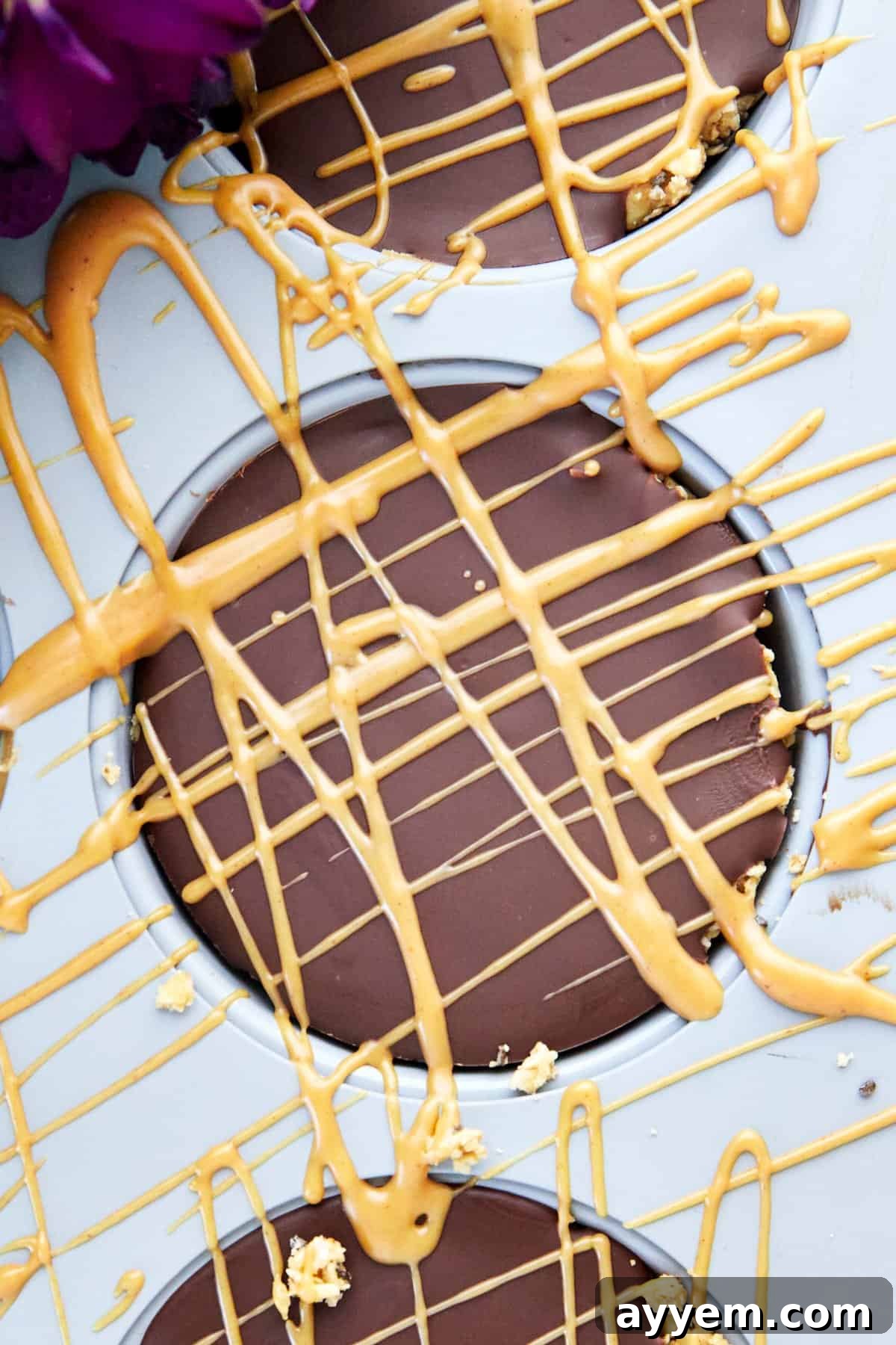 A no-bake peanut butter oat cup in a muffin pan with a fresh drizzle of peanut butter on top of the chocolate layer.