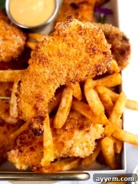 Crispy golden brown chicken tenders on a baking tray, accompanied by a side of fries.