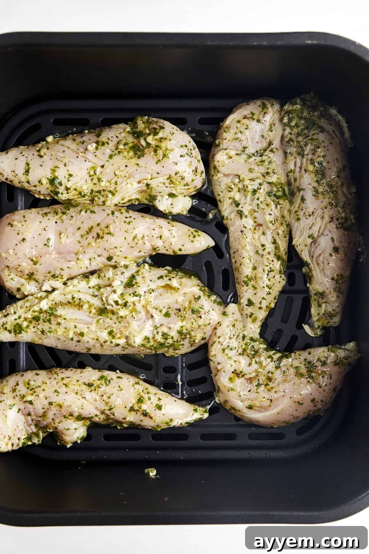Raw marinaded chicken tenders in an air fryer basket. 