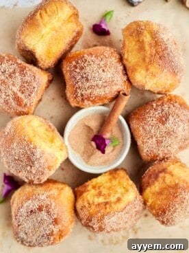 Cinnamon bun air fryer french toast buns on a piece of parchment paper with a bowl of cinnamon sugar in the center