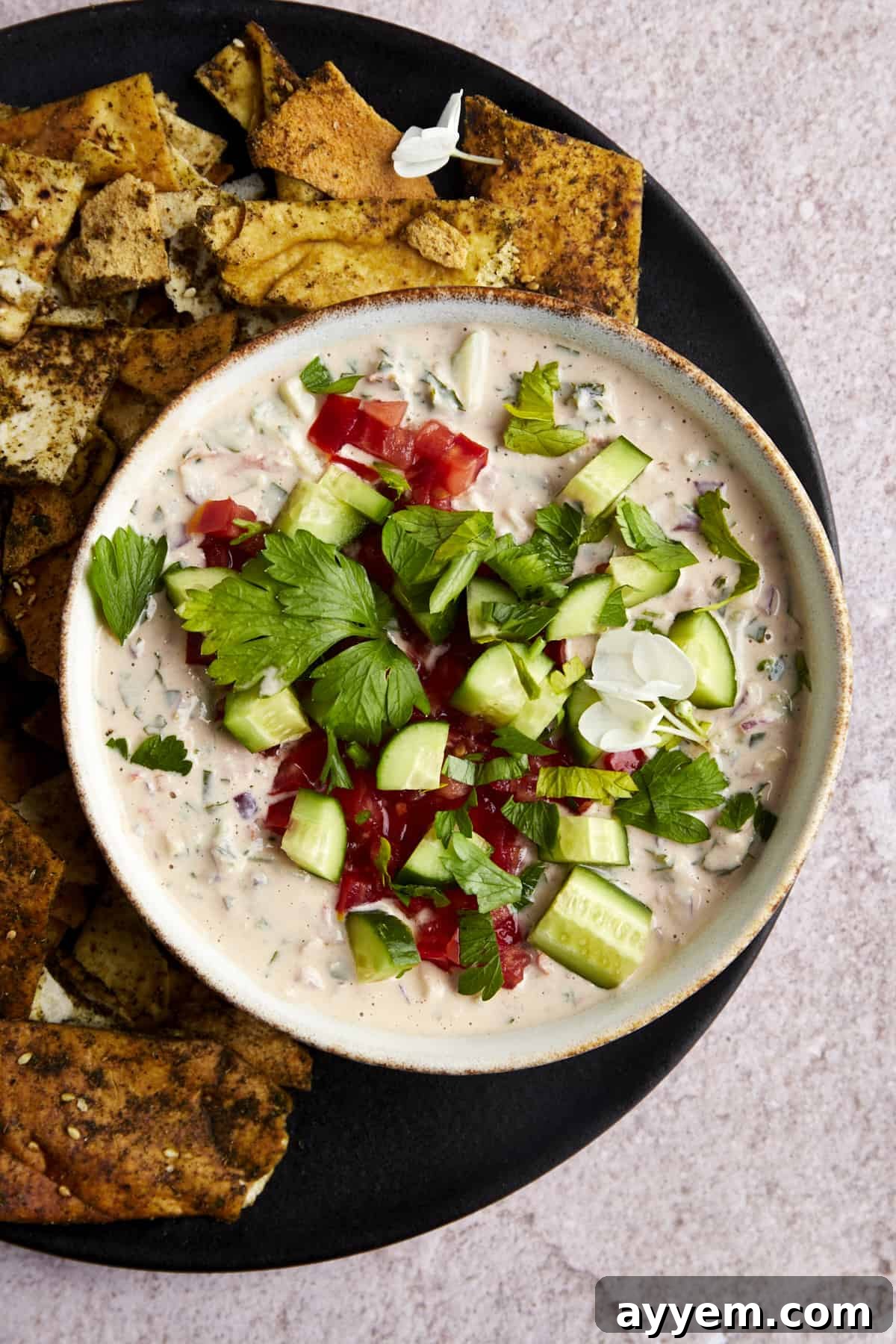 A beautifully arranged bowl of cucumber tomato tahini salad, vibrant with fresh ingredients, with a side of golden pita chips perfect for scooping.