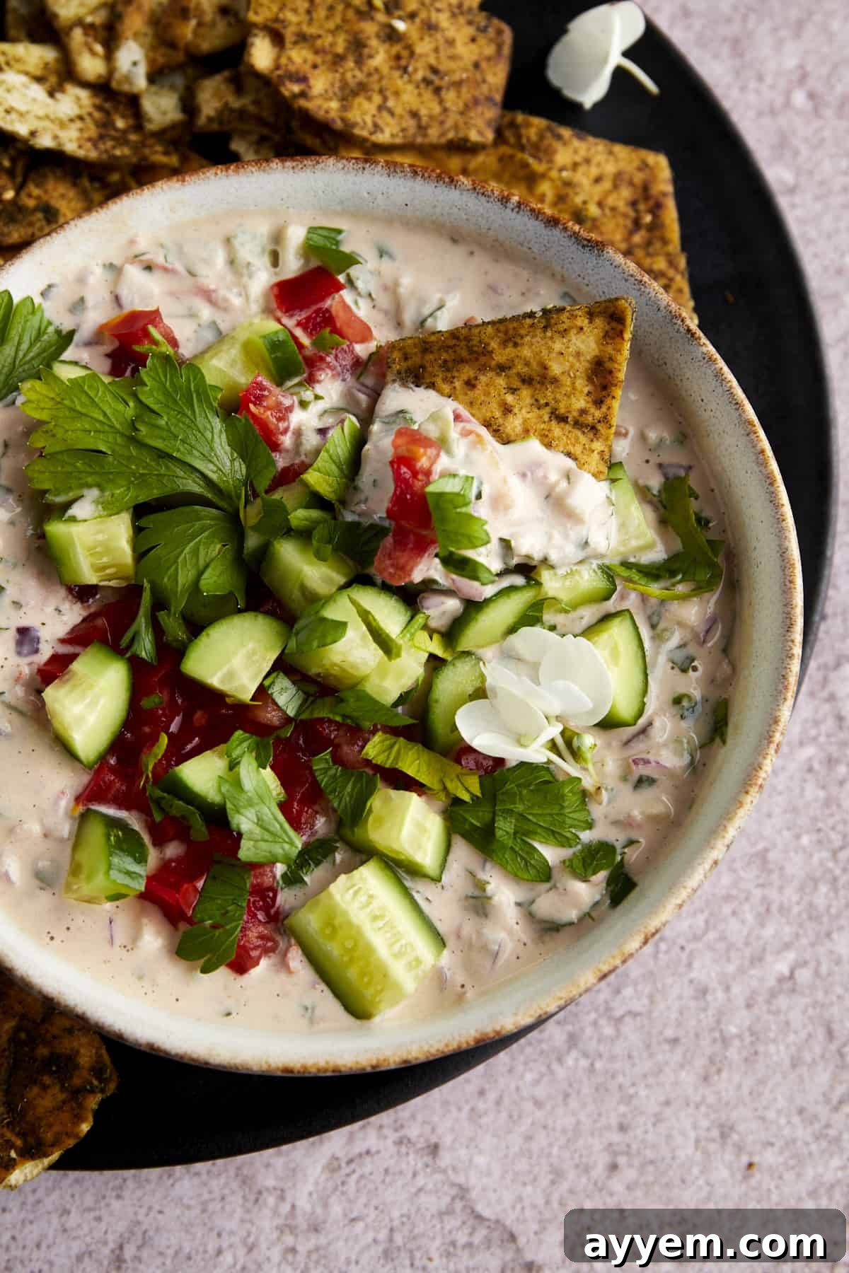 A pita chip dipping into a bowl of tahini salad.