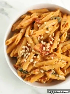 A close-up of a bowl filled with luscious one-pot sun-dried tomato pasta, garnished with fresh herbs and pine nuts.