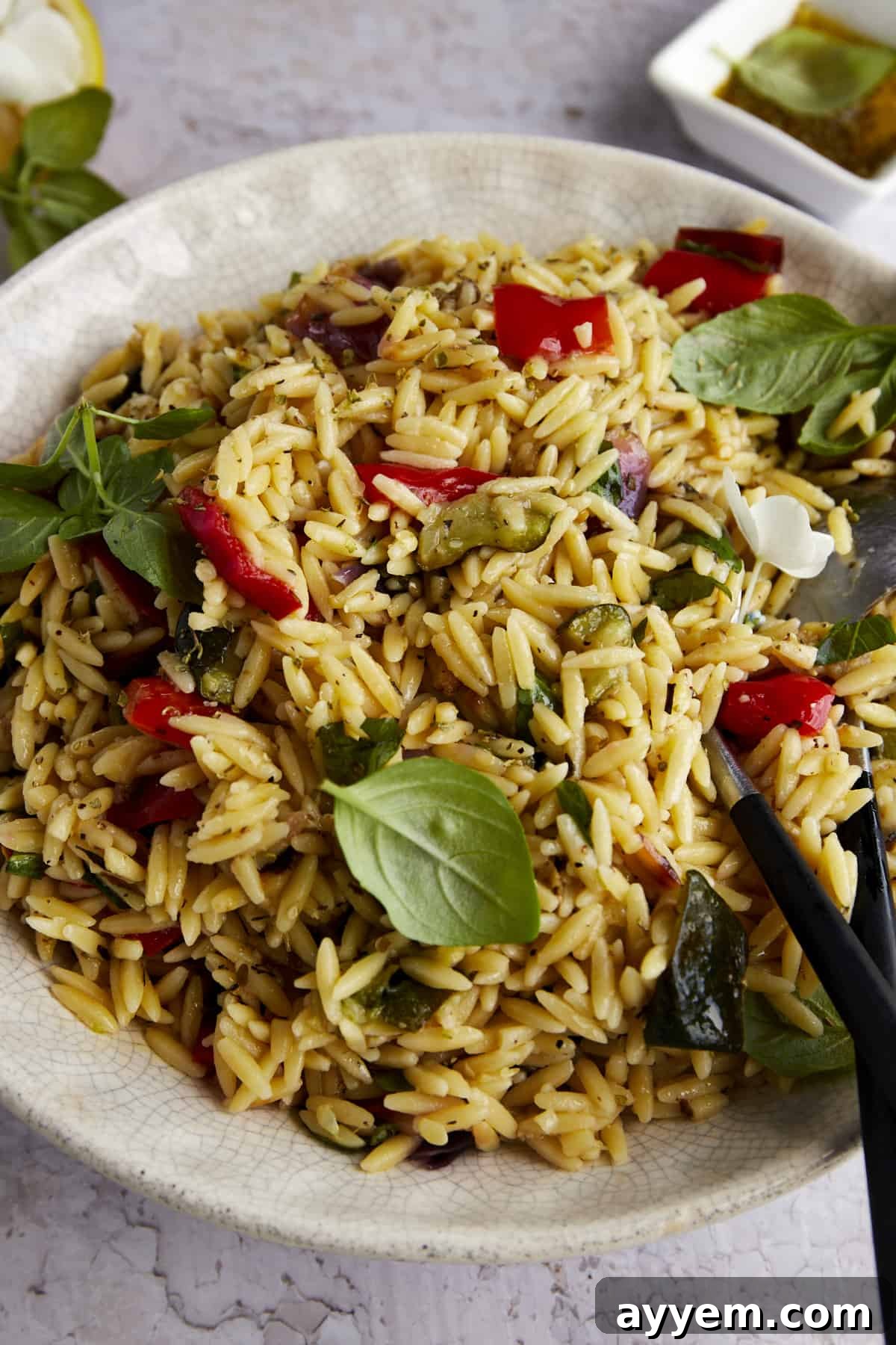 A close-up view of the roasted veggie pasta salad in a white bowl, highlighting the colorful medley of vegetables and orzo pasta, glistening with the zesty dressing.