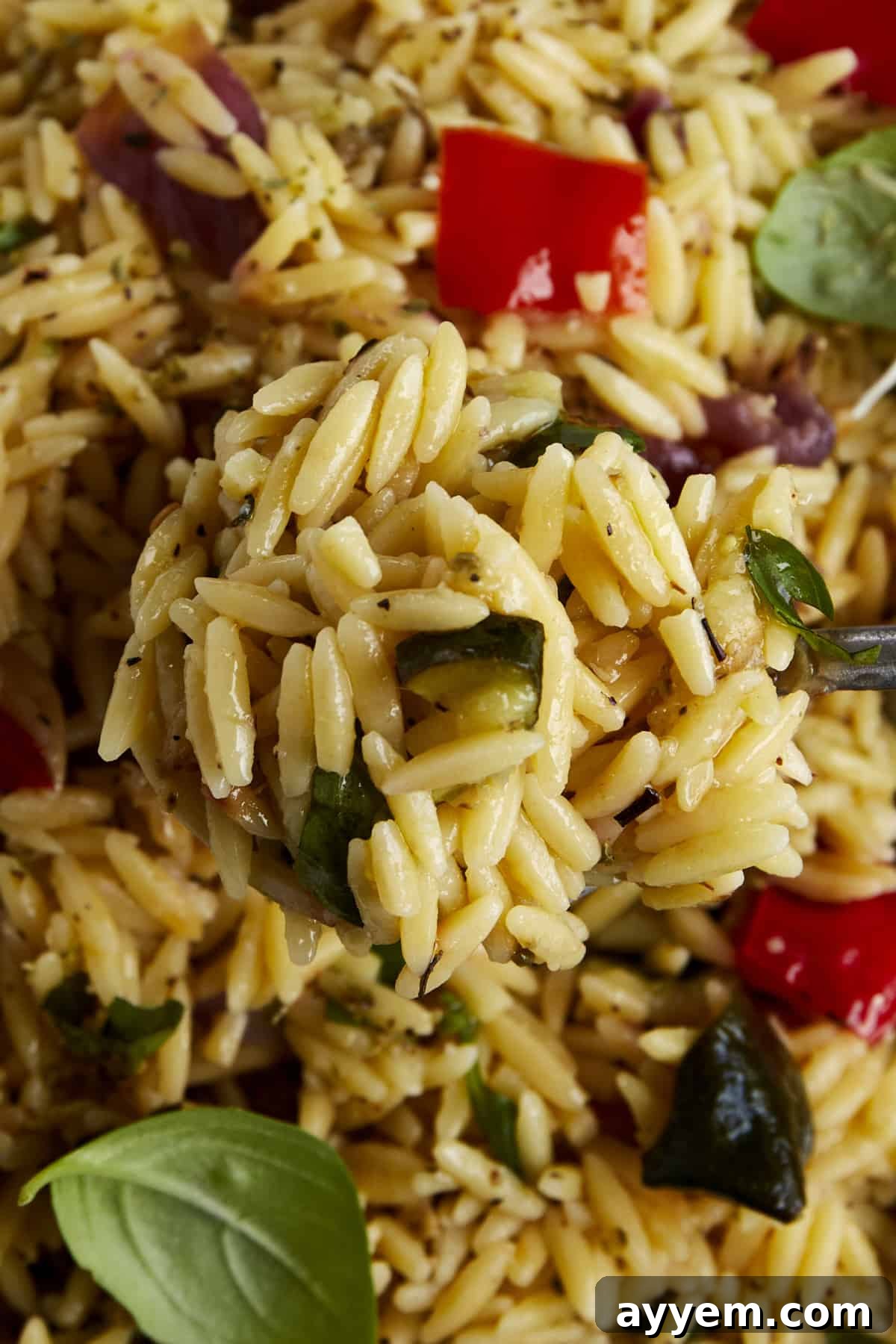 A serving spoon lifting a generous bite of roasted veggie pasta salad, showcasing the individual orzo grains and tender roasted vegetables.