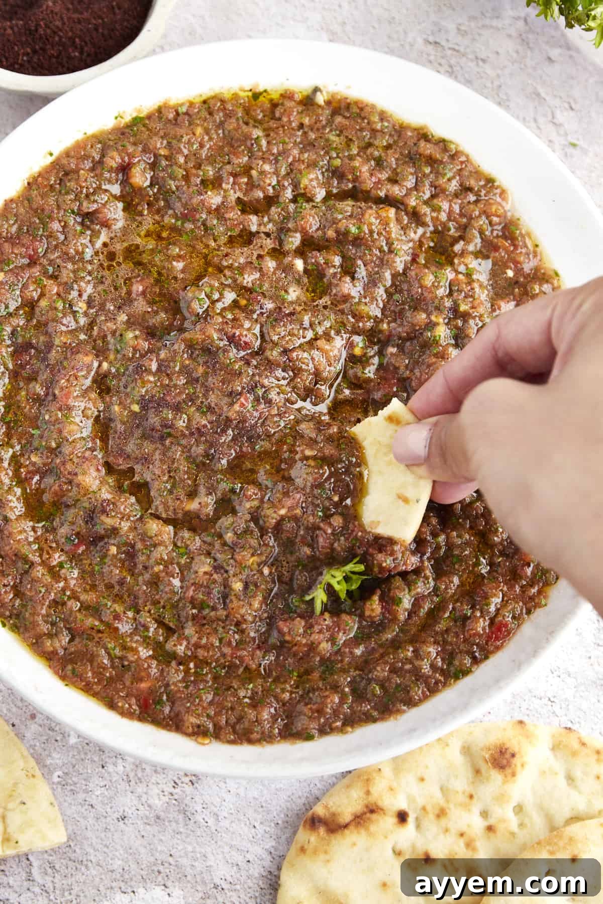  A hand dipping pita bread into a bowl of ezme. 