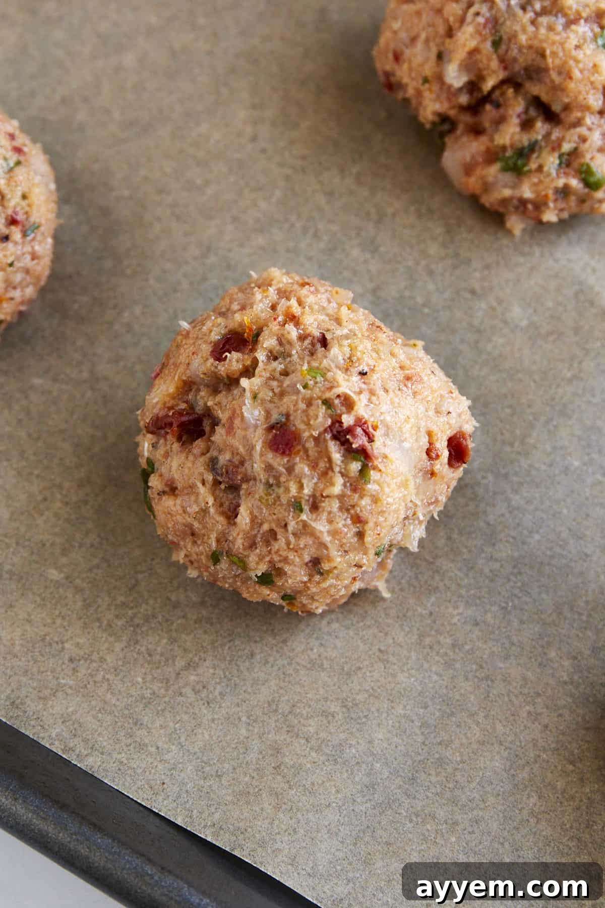 Raw ground chicken meatballs on a parchment paper-lined baking sheet. 