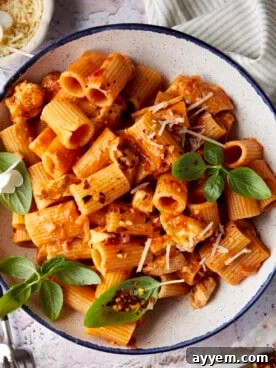 A plate of spicy chicken rigatoni pasta, garnished with fresh herbs and grated cheese.