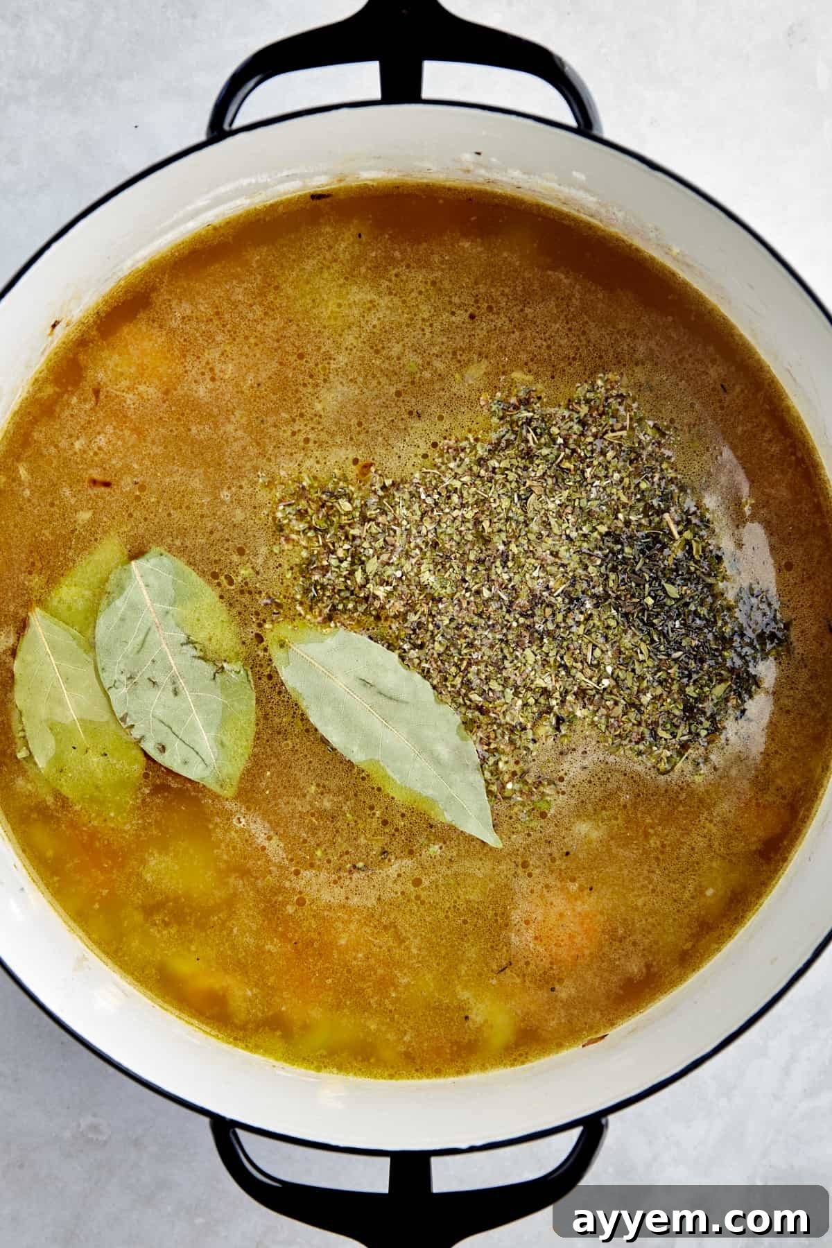 Vegetables, broth, seasonings, and bay leaves in a soup pot. 