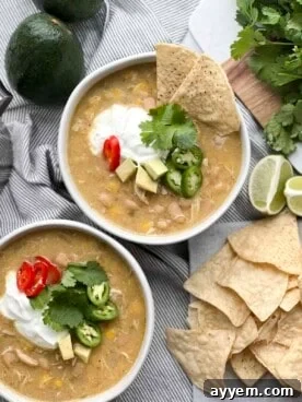 Two bowls of white chicken chili with sour cream, avocado, jalapeño, and tortilla chips.