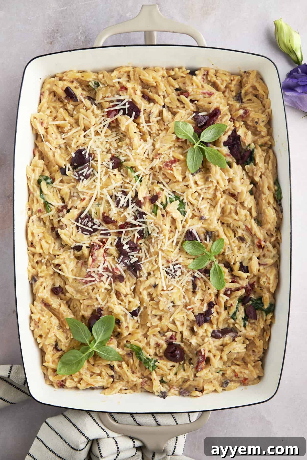 A large baking dish filled with the baked spinach and sun-dried tomato Boursin orzo, glistening with creamy sauce.