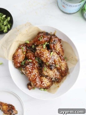 A bowl overflowing with golden, sticky air fryer honey garlic chicken wings, glistening with sauce and topped with sesame seeds.