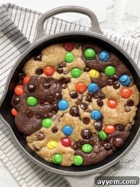 An overhead shot of a warm, gooey M&M brookie skillet, generously studded with colorful M&Ms, fresh from the oven.