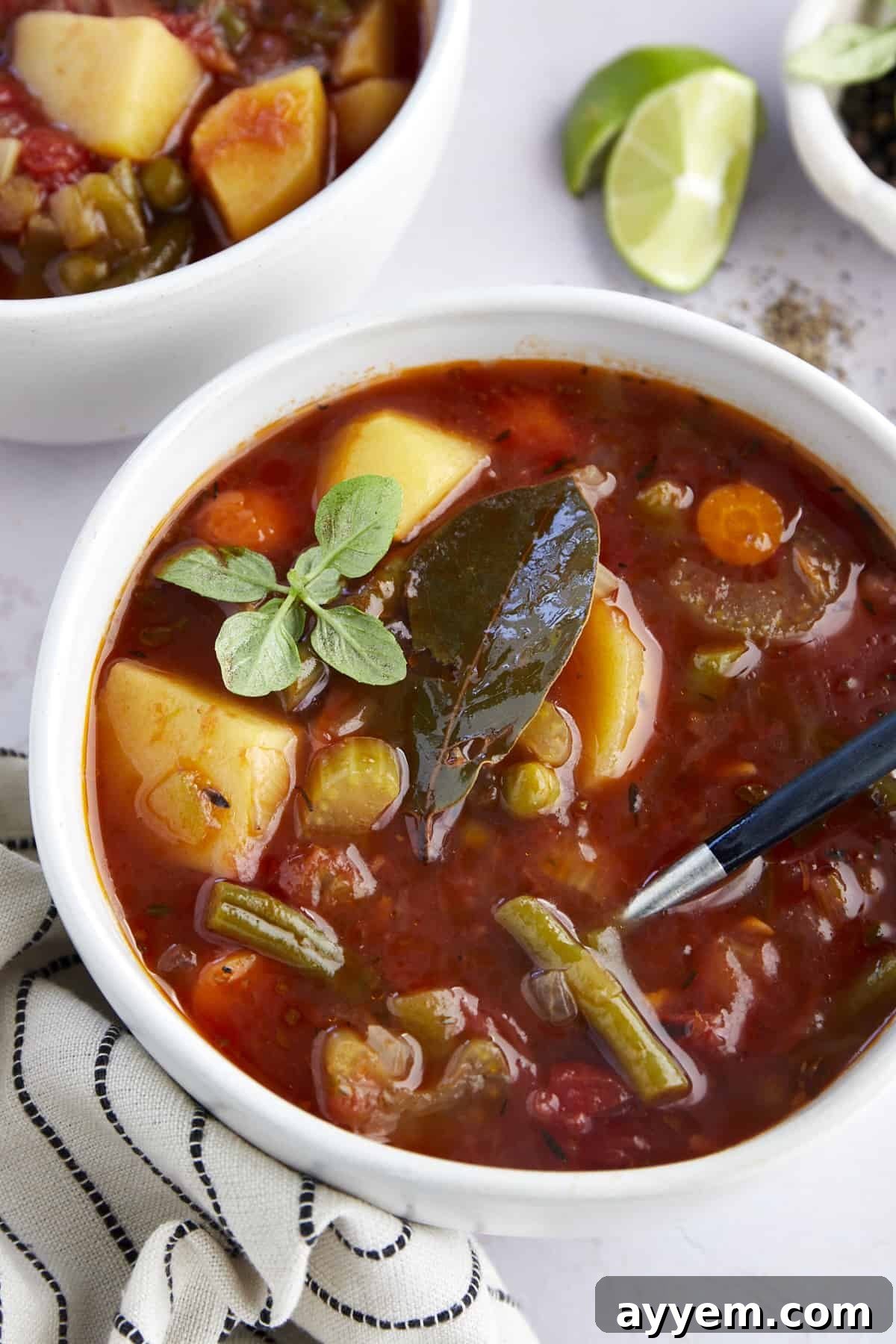 Close up image of a bowl of slow cooker vegetable soup topped with a bay leaf and fresh greens.