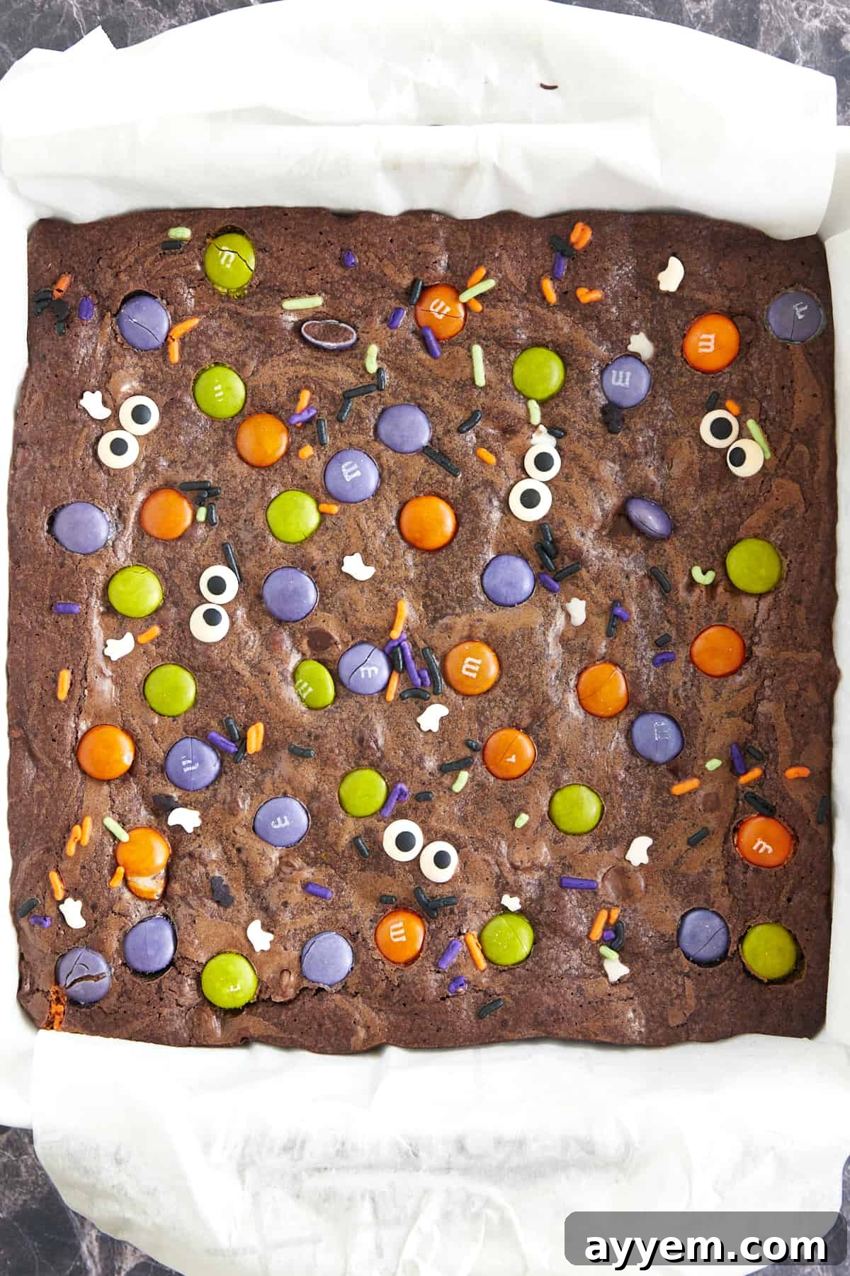 A baking dish full of Halloween brownies topped with M&Ms, sprinkles, and candy eyes. 