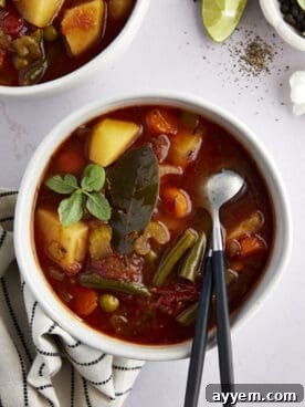 A hearty bowl of slow cooker vegetable soup, brimming with colorful vegetables, with two spoons ready to serve.