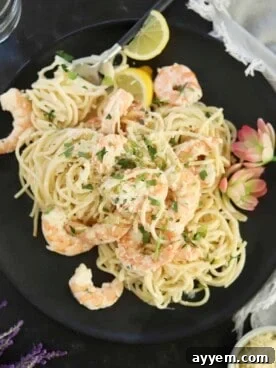 A plate of glistening garlic shrimp scampi, garnished with fresh parsley and lemon slices, with a fork ready to serve.