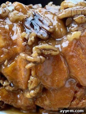 A close-up of warm, sticky baked pecan caramel monkey bread, topped with glaze and chopped pecans.