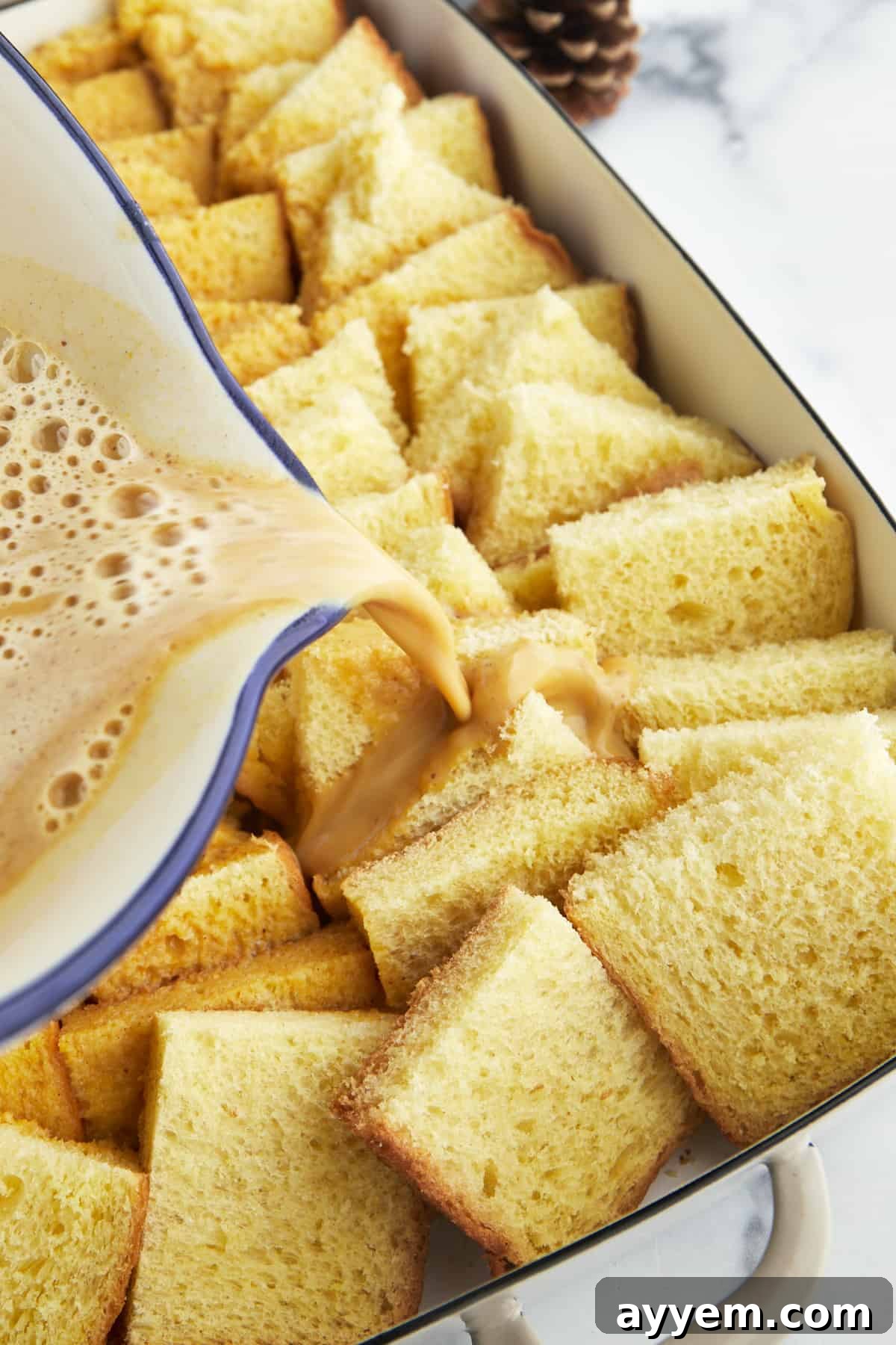 Pouring the creamy pumpkin custard evenly over the bread cubes in the baking dish.
