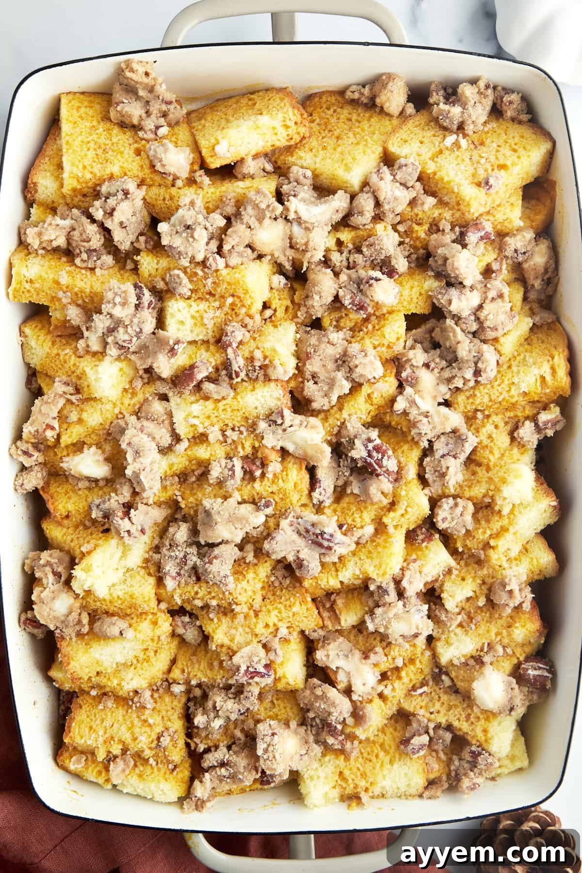 The unbaked pumpkin French toast casserole in a baking dish, generously topped with streusel, ready for chilling.