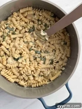 Close-up of creamy spinach artichoke pasta in a bowl, garnished with fresh parsley and parmesan cheese.