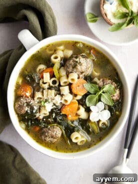 Overhead image of a bowl of hearty Italian wedding soup, garnished with fresh herbs and small meatballs.