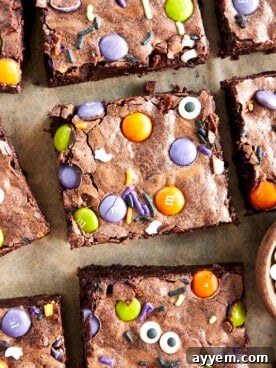 Square Halloween brownies topped with colorful M&Ms, festive sprinkles, and edible candy eyeballs, on a dark background.