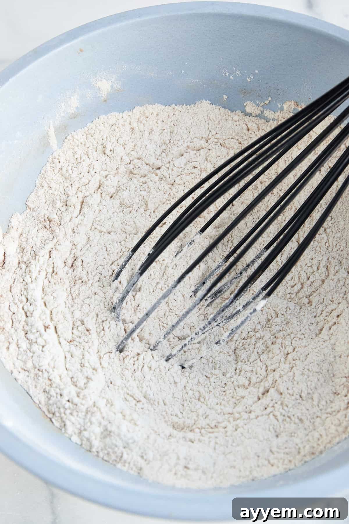 Dry muffin batter ingredients being whisked in a blue bowl. 