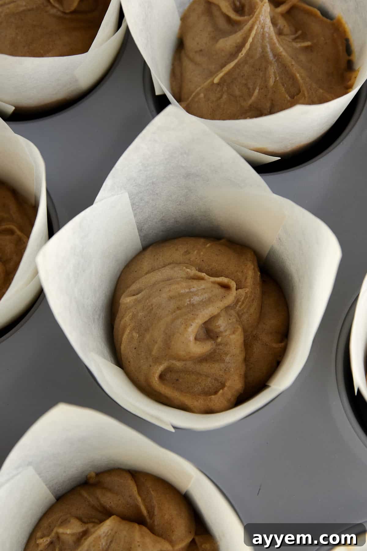 Unbaked apple cider muffins in a muffin tin lined with paper. 