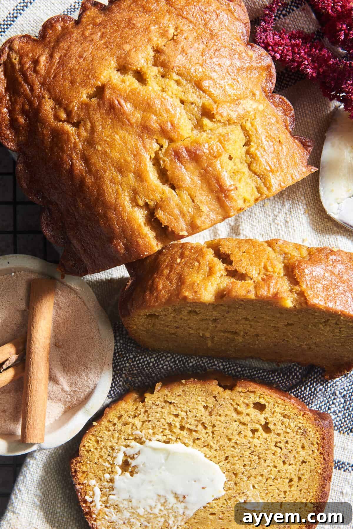 A golden-brown loaf of moist pumpkin banana bread, with two slices already cut and one topped generously with melted butter, sitting on a rustic wooden board, ready to be enjoyed.