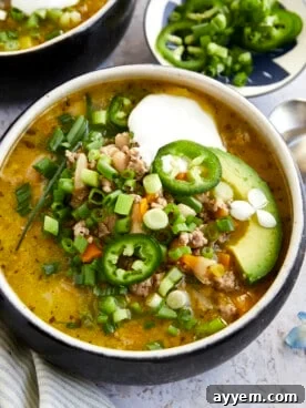 A steaming bowl of healthy white turkey chili topped with sour cream, fresh avocado, sliced jalapeños, and vibrant scallions, perfect for a cozy fall evening.