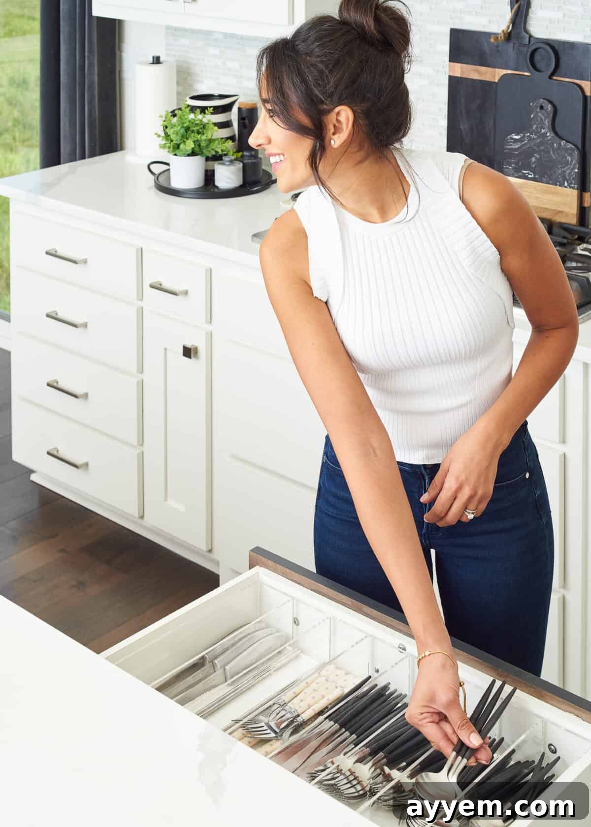 smiling woman placing spoons in drawer organizer of open drawer.