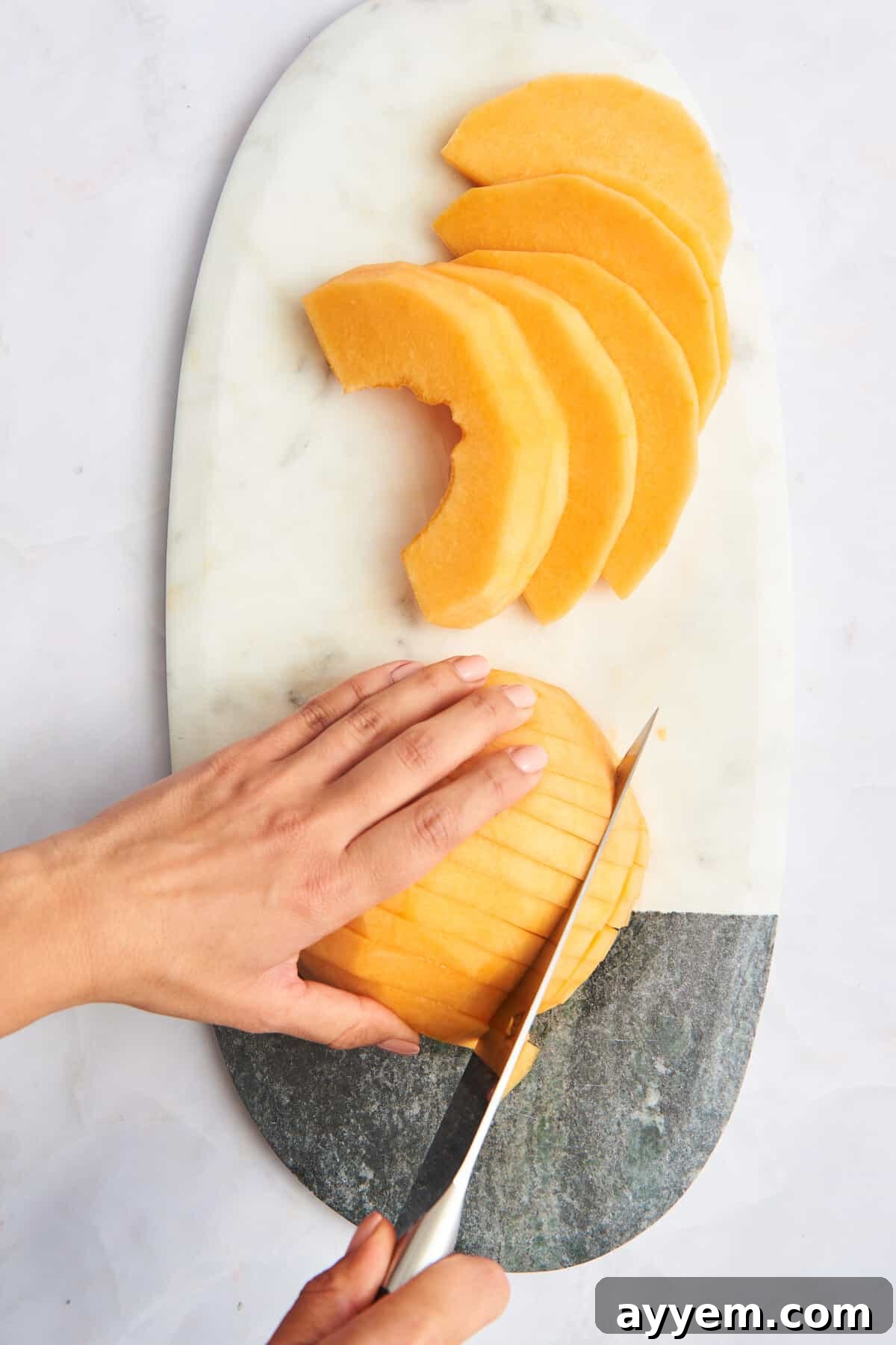 A cantaloupe being expertly sliced into uniform cubes on a cutting board.