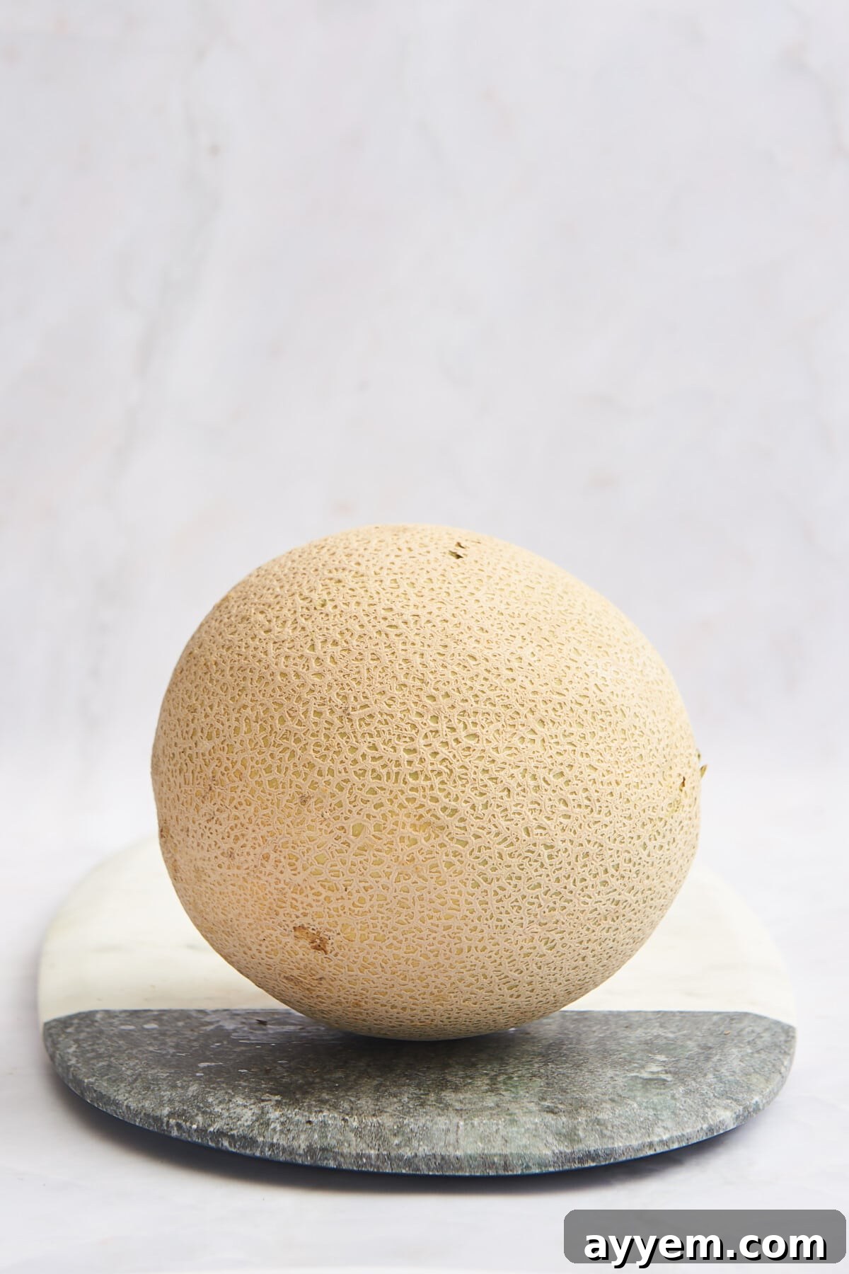 A whole cantaloupe on a cutting board ready to be cut.