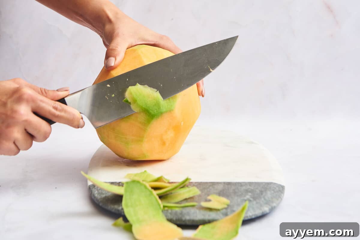 Rind of a cantaloupe being trimmed off, showing the vibrant orange flesh beneath.