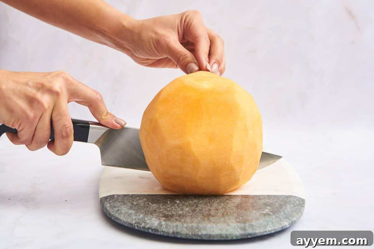 A peeled cantaloupe being carefully cut in half lengthwise.