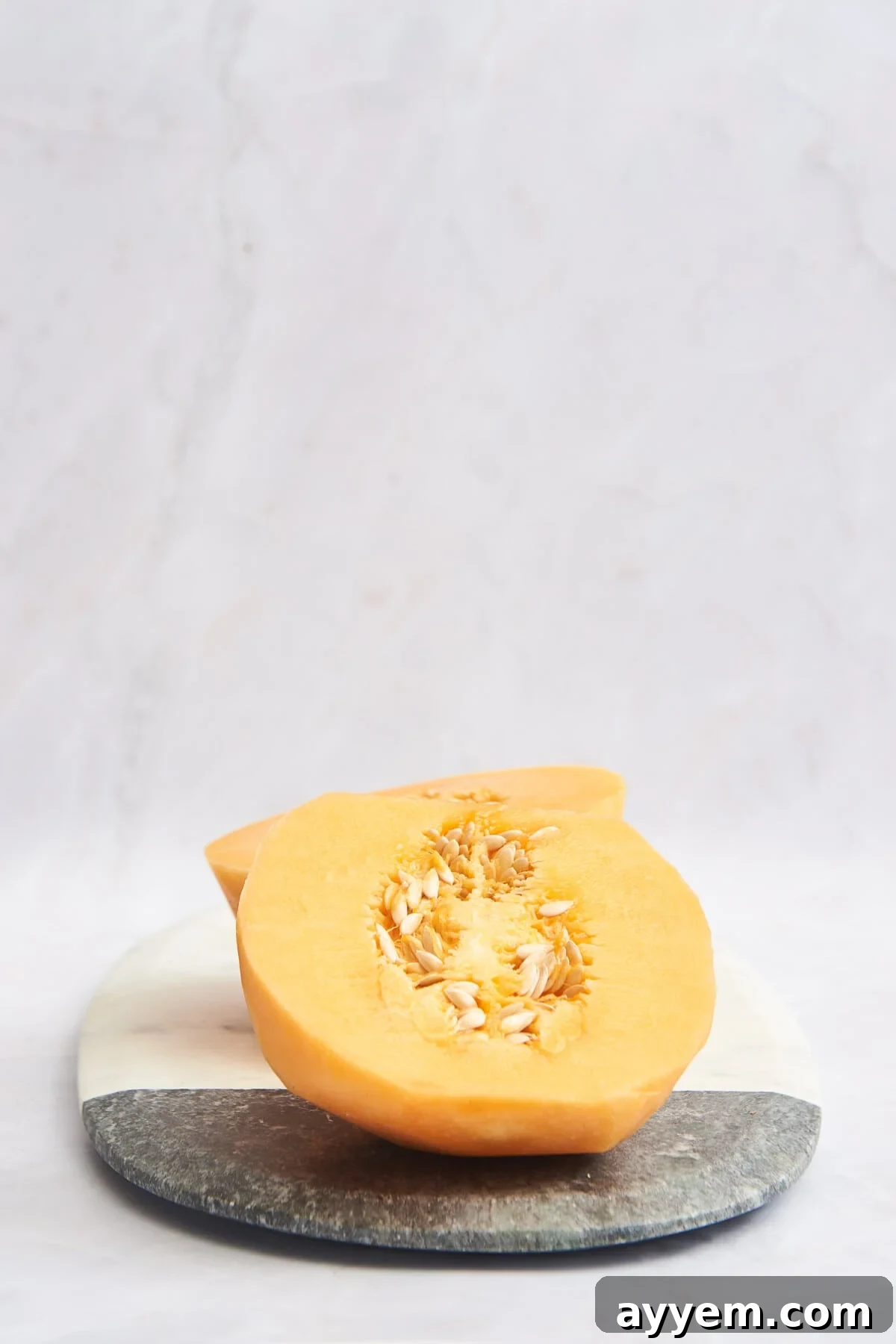 Peeled cantaloupe halves resting on a cutting board, ready for de-seeding.