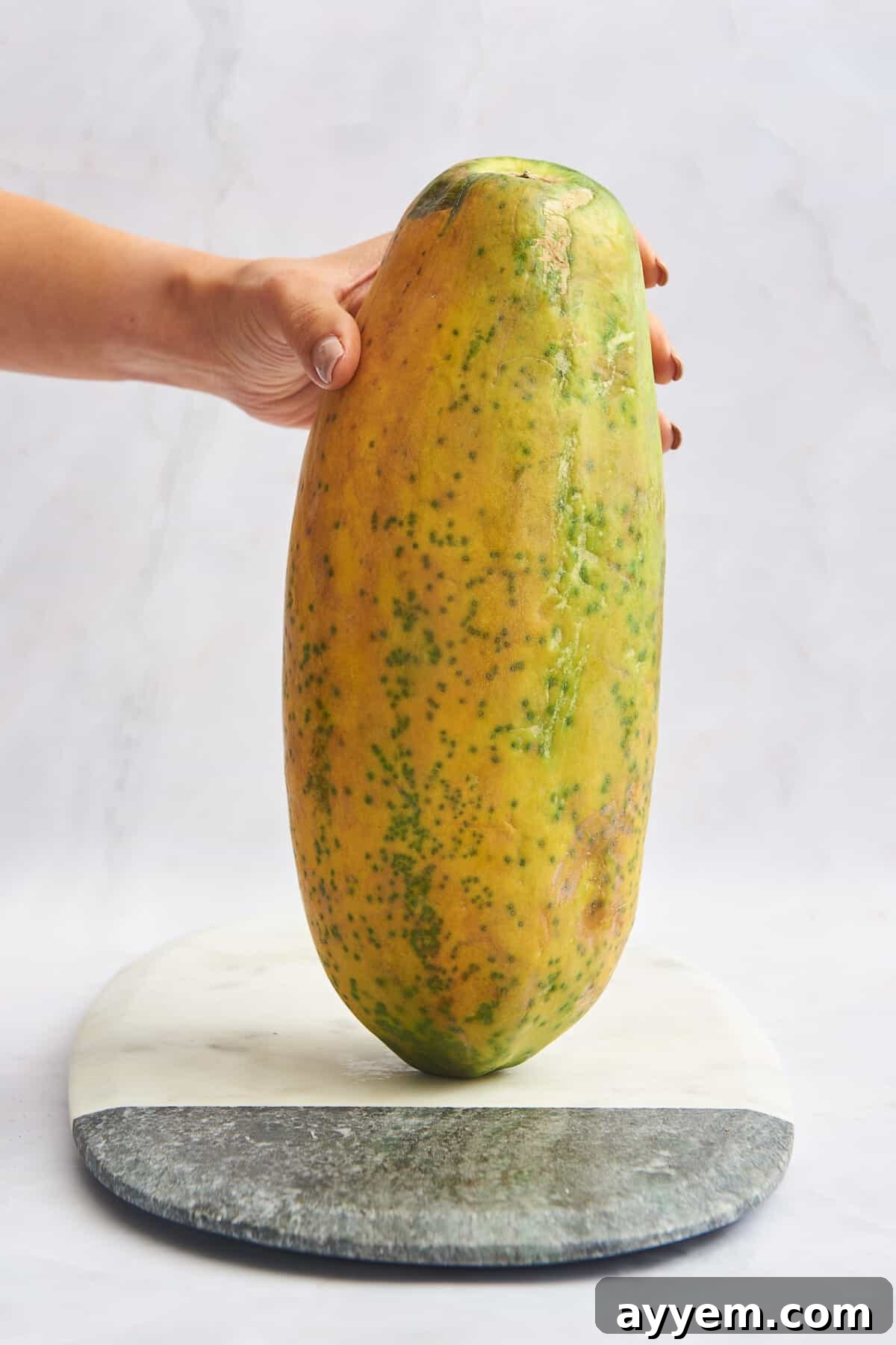 A hand holding a whole papaya.