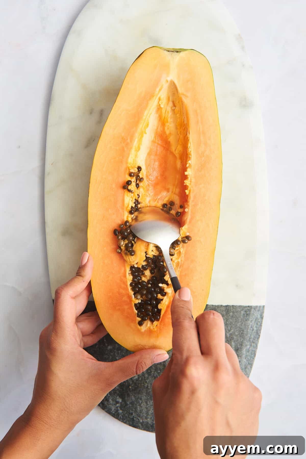 Two hands scooping out the black seeds of a papaya.