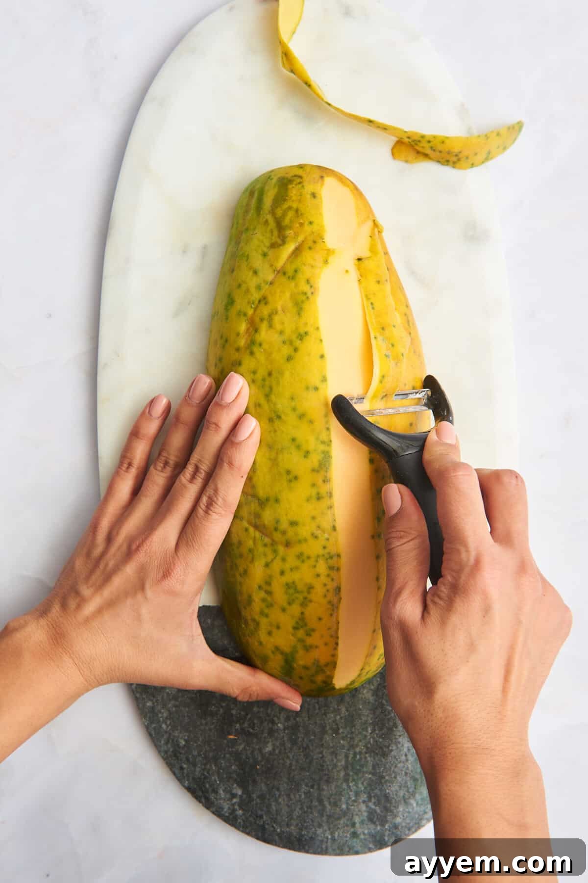 A hand using a vegetable peeler to remove the skin from a papaya.