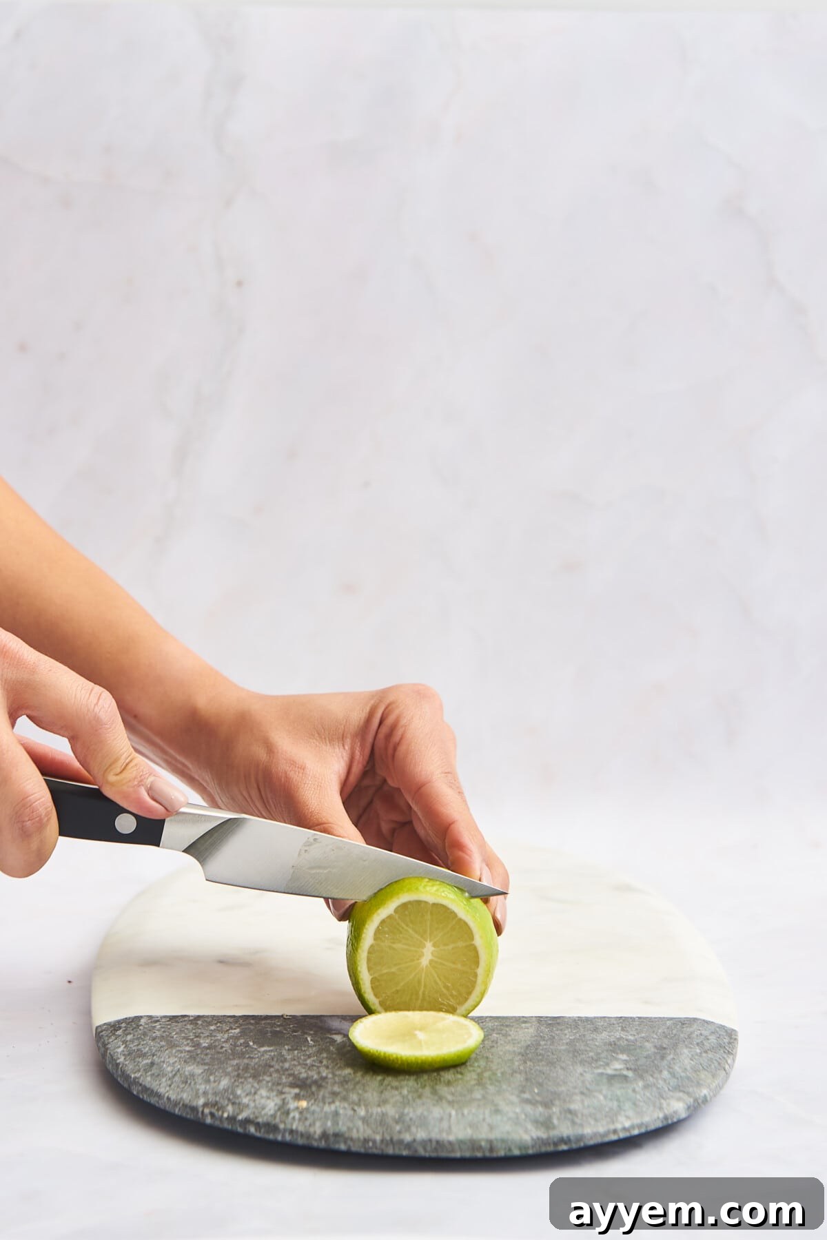 A lime being sliced into perfect rounds on a marble cutting board, highlighting the thin, even cuts.