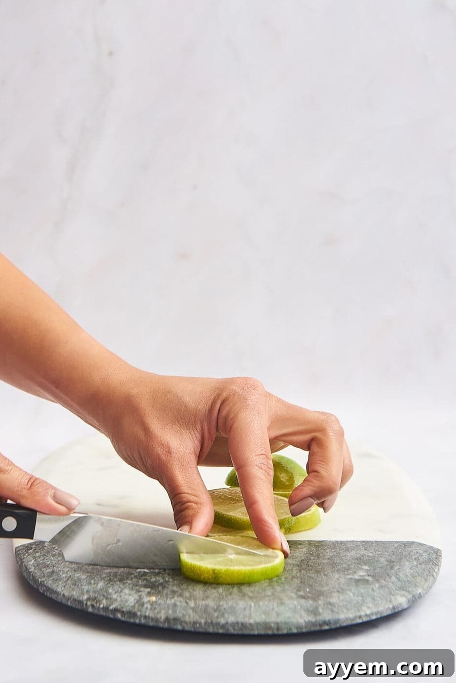 Lime rounds being sliced in half on a marble cutting board, demonstrating the versatility of lime cuts.