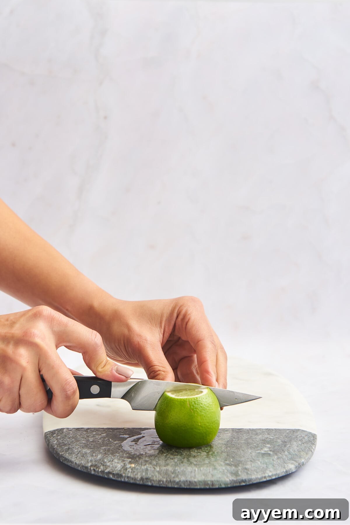 A lime being sliced in half on a marble cutting board, demonstrating the initial step for wedges.